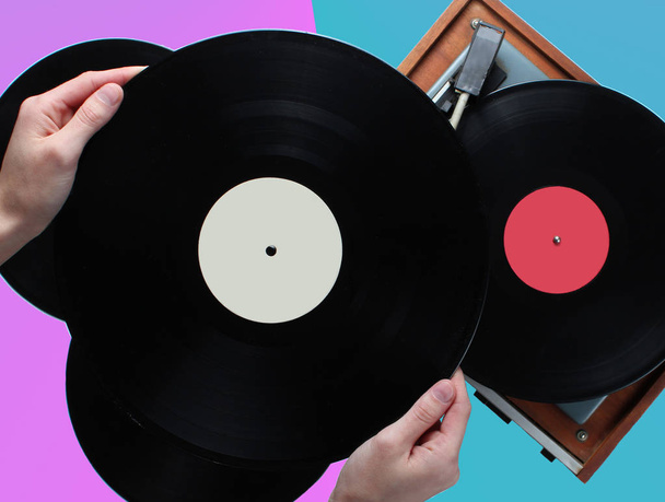 Ženská ruka držící vinylový rekord, vinylový hráč se záznamy na dvoubarevném pozadí. Retro styl, 80, pohled shora - Fotografie, Obrázek