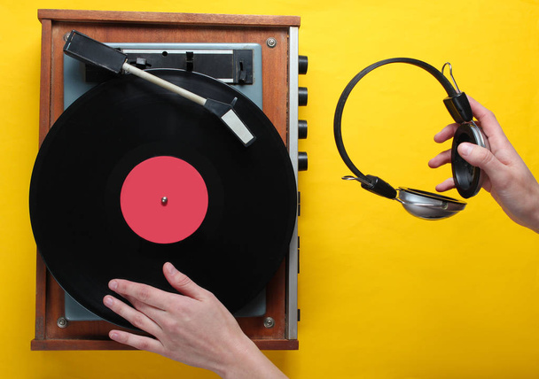 Styl retro, DJ odgrywa odtwarzacz płyt winylowych i trzyma słuchawki w ręku, minimalizm, widok z góry na żółtym tle - Zdjęcie, obraz