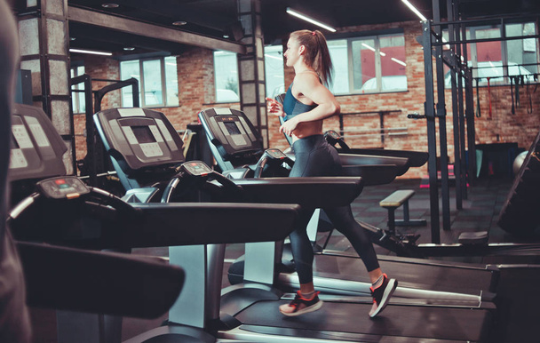 Mujer deportiva joven haciendo entrenamiento cardiovascular en la cinta de correr. Correr en la cinta de correr en el gimnasio. - Foto, Imagen