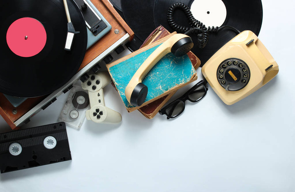 Retro 80s pop culture objects on white background. Copy space. Rotary phone, vinyl player, old books, audio, video tapes, 3d glasses, gamepad. Top view. - Photo, Image