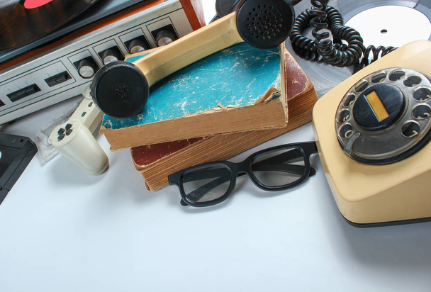 Retro 80s pop culture media objects on white background. Copy space. Sneakers, rotary phone, vinyl player, old books, audio, video tapes, 3d glasses, gamepad. - Photo, Image