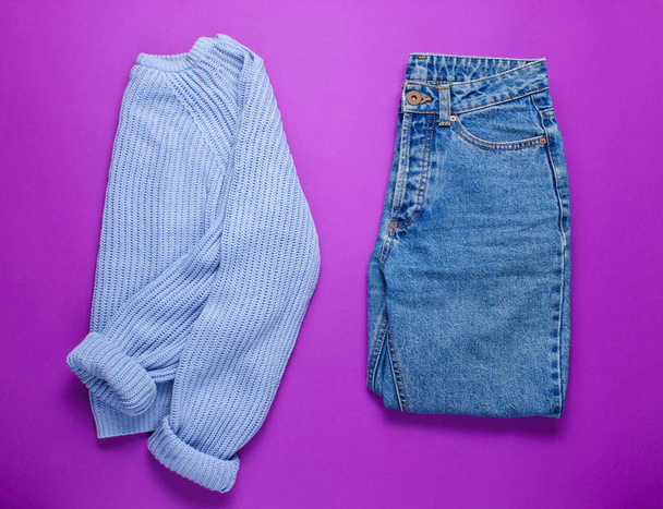 Jeans und Pullover für Frauen auf lila Hintergrund. Ansicht von oben. Minimalismus - Foto, Bild