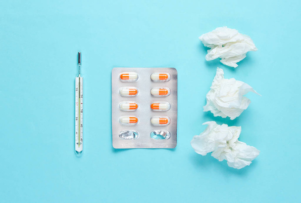 The concept of treating cold diseases. Used nasal wipes, thermometer, pills on orange background. Top view - 写真・画像