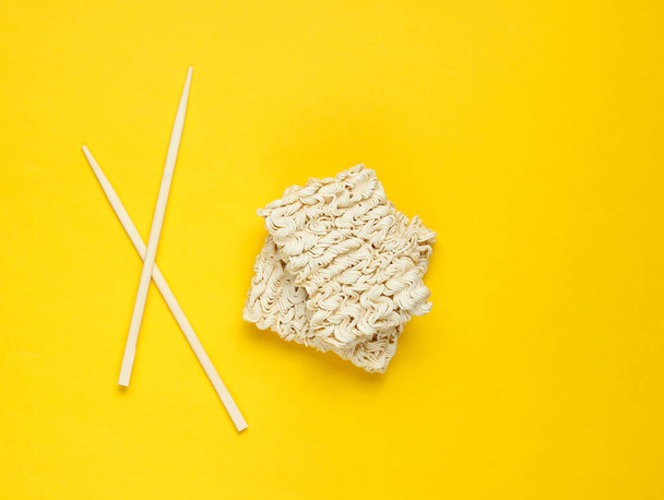 RAW instant noedels en Chinese eetstokjes op gele achtergrond, minimalisme. Top View - Foto, afbeelding