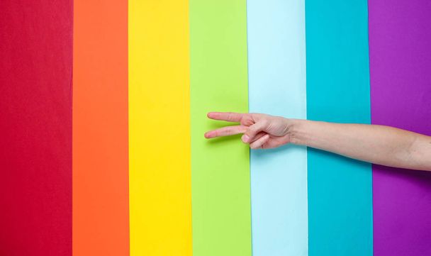 Concepto LGBT. Sexo minoritario. Mano mostrando signo de paz en el fondo del arco iris. Vista superior, minimalismo
 - Foto, imagen