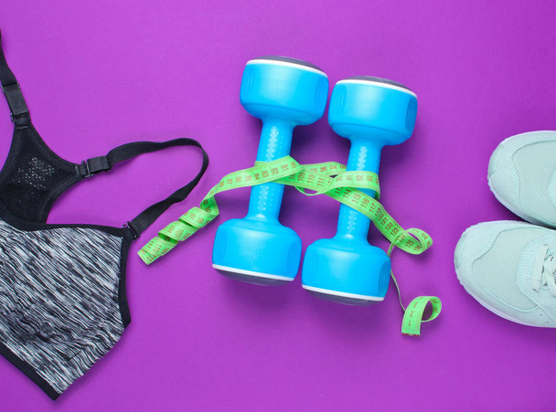 Fitness concept. Weight loss. Sports bra,shoes, dumbbells, ruller on purple background. Top view, flat lay - Photo, Image