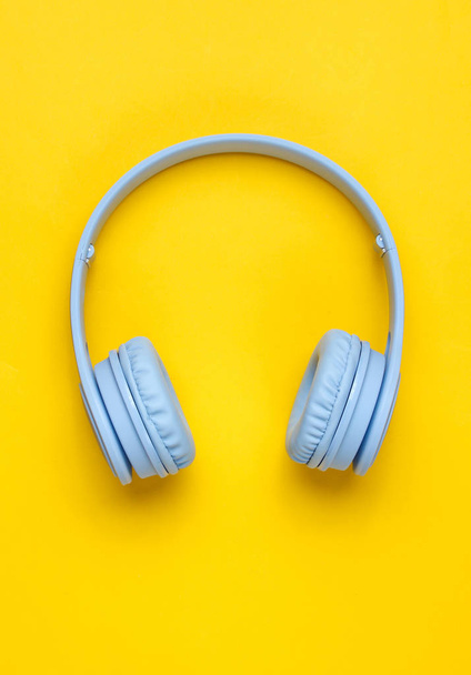 Moderne draadloze over-ear blauwe hoofdtelefoon op gele achtergrond. Minimalisme. Top View - Foto, afbeelding