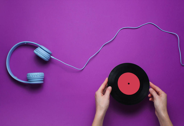 Les mains des femmes détiennent un disque vinyle sur fond violet avec un casque au-dessus de l'oreille. Pop culture, style rétro, années 80. Minimalisme. Vue de dessus. Pose plate - Photo, image