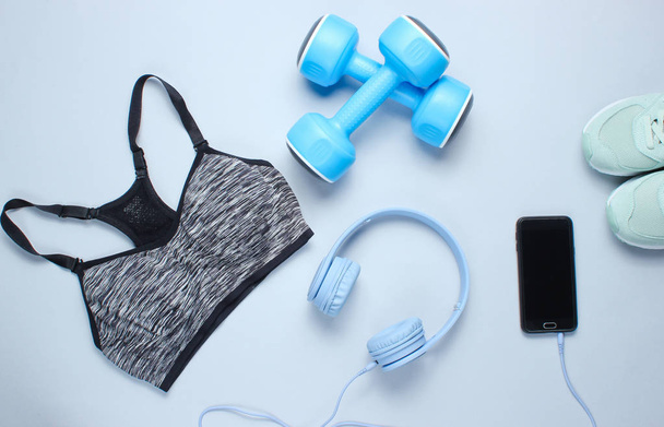 Concept de fitness. Pose plate d'un smartphone avec écouteurs, haltères en plastique, soutien-gorge de sport, baskets sur fond gris. Vue du dessus
 - Photo, image