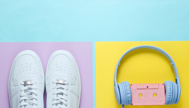 Beyaz spor ayakkabılar, kulaklıklar ve ses kaseti. Renkli arka planda 80 'lerin modası geçmiş nesneler. Üst Manzara. Düz yatıyordu. - Fotoğraf, Görsel