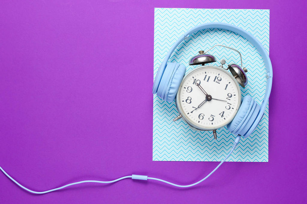Čas poslouchat hudební koncepci. Retro Budík s kabelovými sluchátky na fialově modrém pozadí. Pohled shora - Fotografie, Obrázek