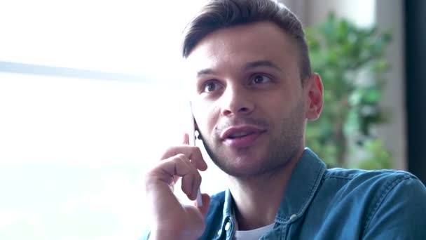 Conversation with friend. Communication it's easy. Close up portrait of handsome smiling man in jeans clothes while he talks on phone at home. Modern business man. - Кадри, відео