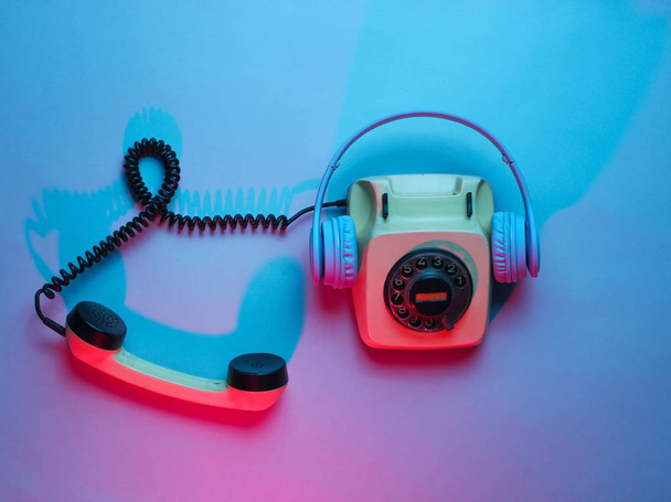 Vintage rotary phone with headphones. Retro wave, red blue neon light, ultraviolet. Top view, minimalism - Foto, immagini