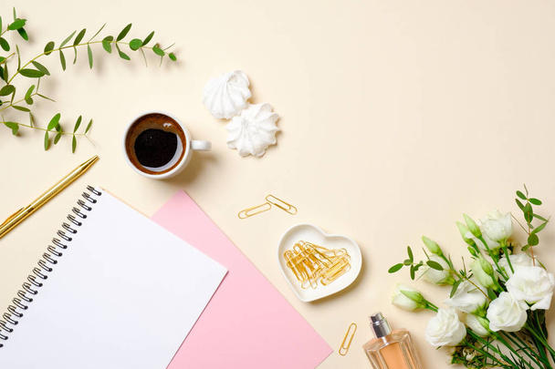 Flat lay home office desk, top view. Feminine accessories on pastel beige background. Coffee cup, paper notepad, golden paper clip, roses flower bouquet. Women home office desk, beauty blogger diary - Фото, изображение