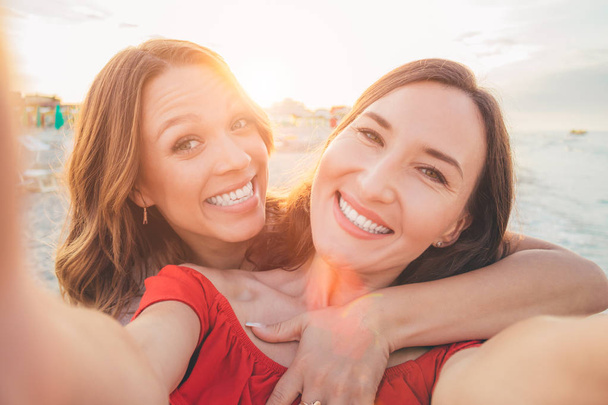 Two smiling girlfriends making a selfie on the beach - Foto, afbeelding
