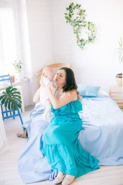 Young mother and little cute baby at home on bed with blue bedspread and pillows - Foto, immagini