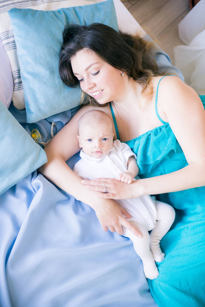 junge Mutter und kleines süßes Baby liegen zu Hause auf einem Bett mit einer blauen Decke - Foto, Bild