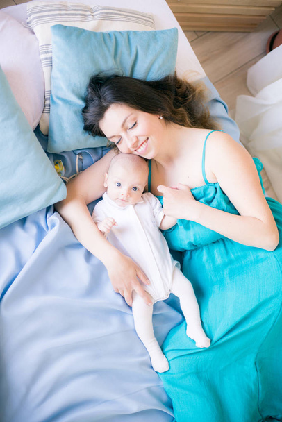 Young mother and little cute baby lying on a bed with a blue blanket at home - Foto, imagen