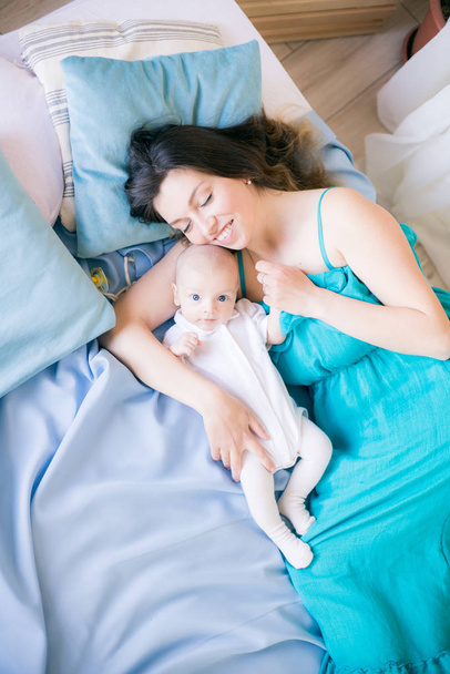 Nuori äiti ja pieni söpö vauva makaa sängyllä, jossa on sininen huopa kotona
 - Valokuva, kuva