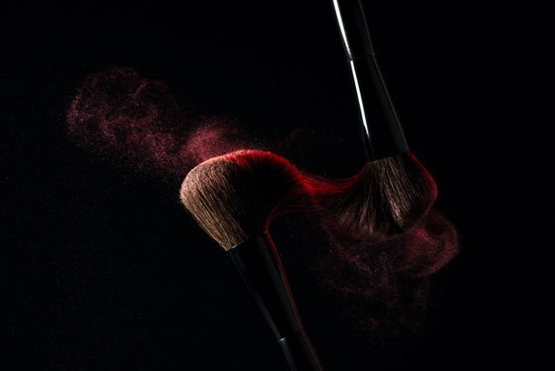Cepillo de maquillaje con explosión de polvo sobre fondo negro
 - Foto, imagen