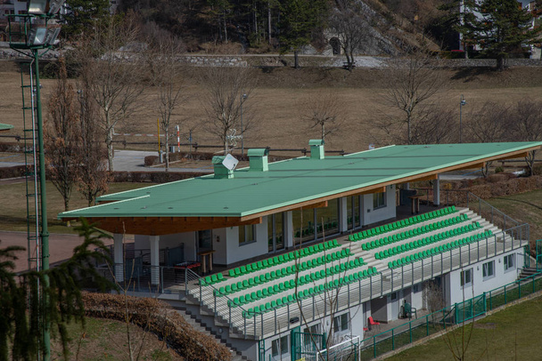 Petit stand de spectateur d'un terrain de football avec des sièges verts. Tribuns vides d'un petit stade moderne sans spectateurs et chaises colorées à Molveno, Trentin, Italie
. - Photo, image