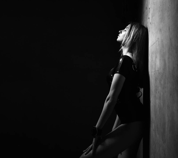 Young beautiful sexy brunette woman in black modern leather cloth posing in dark room - Фото, зображення