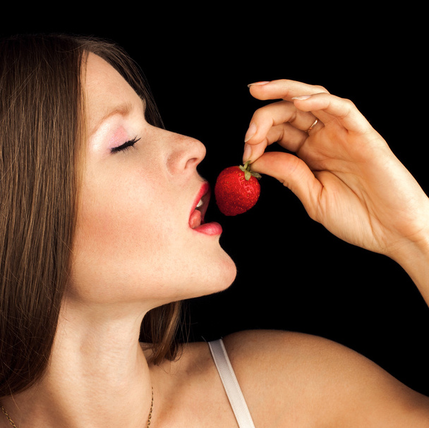 Sexy Woman Eating Strawberry. Sensual Red Lips. Red Nails and Lipstick. Desire. Sexy red Lips with Berry isolated on Black - 写真・画像