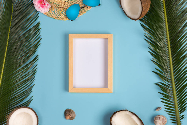 Stylish summer composition with photo frame, green leaves, hat and sunglasses on a blue pastel background. Artwork mockup with copy space - Φωτογραφία, εικόνα