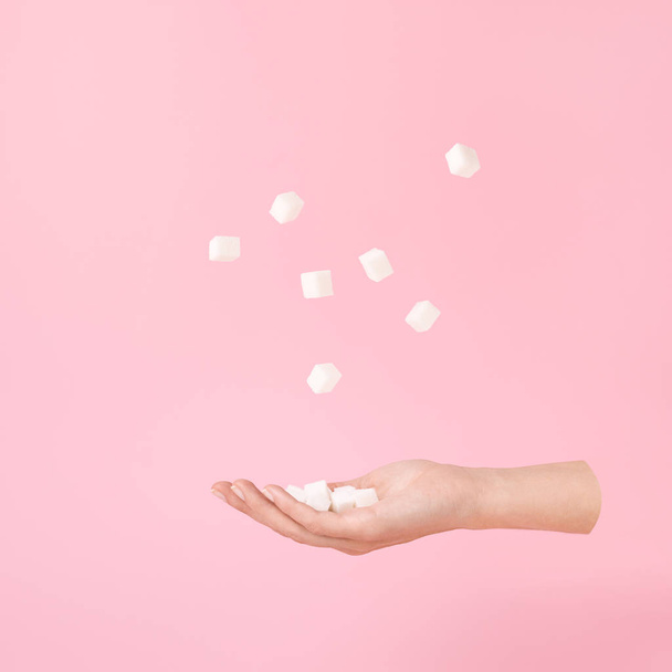 Mano voladora y cubos de azúcar levitación sobre rosa Estilo minimalista o surrealista
. - Foto, imagen