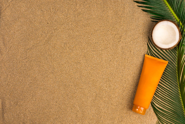 Beach theme on the sand background. Palm leaves, coconut, sunscreen on the sand. Top view. - Fotografie, Obrázek