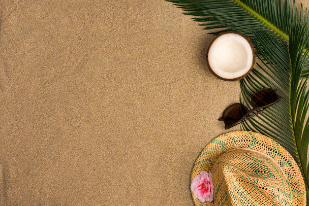  Beach theme on the sand background. Palm leaves, coconut, sunglasses on the sand. Top view. - Photo, Image