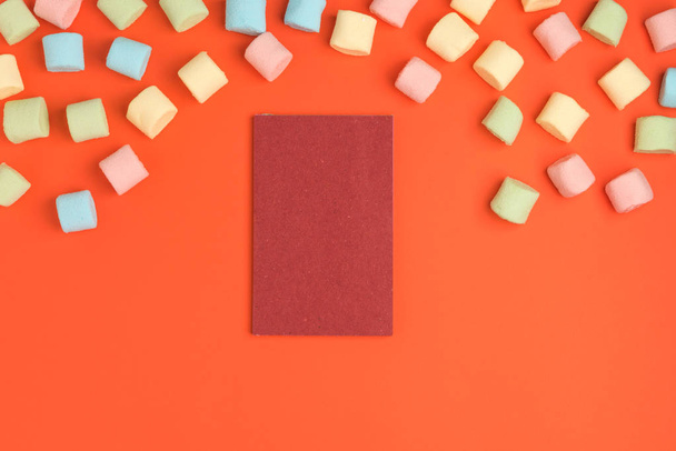 Coral paper background with marshmallow and blank notepad. Place for your text. Cozy sweet background - 写真・画像