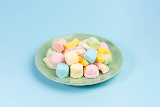 Green plate with marshmallow isolated on blue background. - 写真・画像
