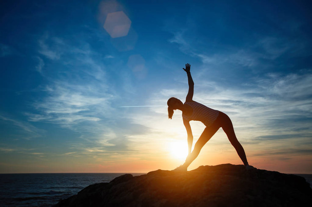 Silhouette einer jungen Frau, die während des Sonnenuntergangs am Meeresstrand Übungen macht. Yoga, Fitness und ein gesunder Lebensstil. - Foto, Bild