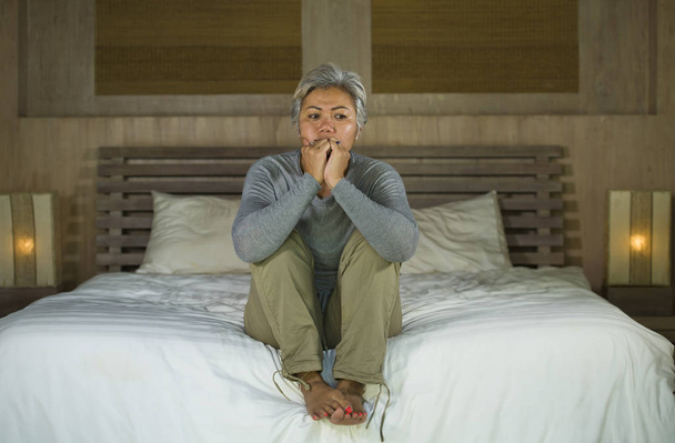 dramatic lifestyle home portrait of attractive sad and depressed middle aged woman with grey hair on bed feeling upset suffering depression and anxiety - Foto, imagen