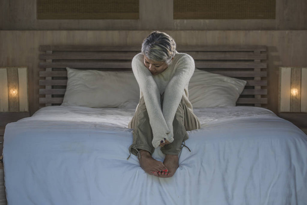 δραματική ζωή σπίτι πορτρέτο της ελκυστική λυπημένη και χαμένη μεσήλικες γυναίκα με γκρίζα μαλλιά κάθονται στο κρεβάτι νιώθοντας απογοητευμένοι υποφέρουν κατάθλιψη και τον πόνο - Φωτογραφία, εικόνα