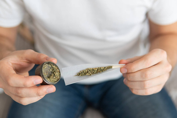 marijuana use concept. Man preparing and rolling marijuana cannabis joint. Man rolling a cannabis joint on white background. Close up of marijuana joint with grinder. - Photo, image