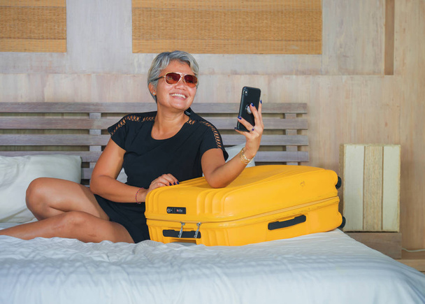 φυσικό στυλ lifestyle πορτρέτο του Happy και ελκυστική 40s να 50s ώριμη Ασιατική τουριστική γυναίκα με γκρίζα μαλλιά φτάνοντας στο δωμάτιο του ξενοδοχείου σε επαγγελματικό ή ταξίδι διακοπών χρησιμοποιώντας το κινητό τηλέφωνο - Φωτογραφία, εικόνα