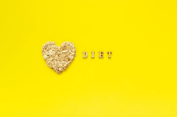 Text Diet and oat flakes in shape heart on yellow background. - Fotó, kép