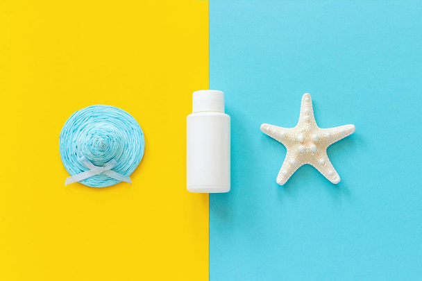 Blue straw hat, starfish and white tube, bottle of sunscreen on yellow and blue paper background. Mock up Template for lettering, text or your design Creative Top View - Φωτογραφία, εικόνα
