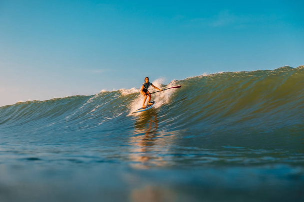 2019. április 12. Bali, Indonézia. Állj fel evezz szörfös lovagolni az óceán hullám. Állj fel lapát szörfözés a hullámok Bali - Fotó, kép