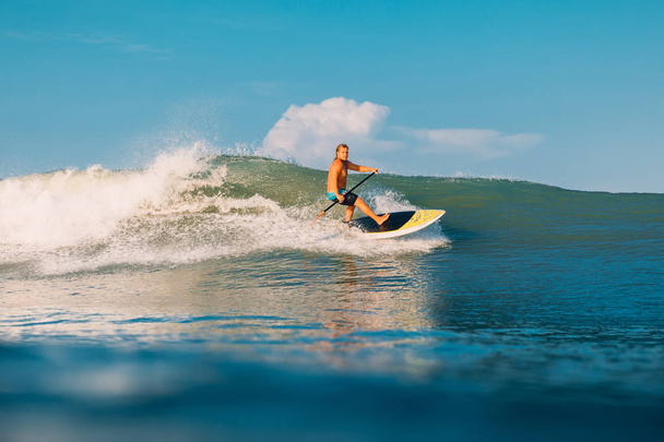 2019年4月12日インドネシア、バリ島。海の波に乗ってパドルサーファーを立ち上がる。バリ島の波でパドルサーフィンを立ち上がる - 写真・画像