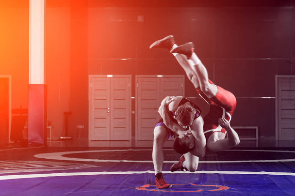 Dva mladíci v modré a červené zápas punčocháče jsou wrestlng a dělat hip hodit na žlutém zápas koberec v tělocvičně. Koncept veletrhu wrestling - Fotografie, Obrázek