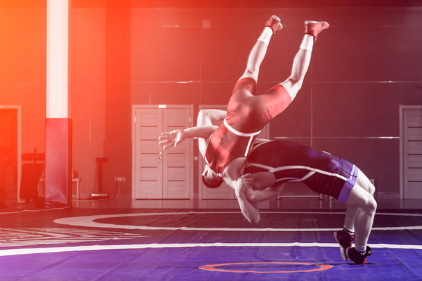 Dva mladíci v modré a červené zápas punčocháče jsou wrestlng a dělat suplex zápas na žlutém zápas koberec v tělocvičně. Koncept veletrhu wrestling - Fotografie, Obrázek
