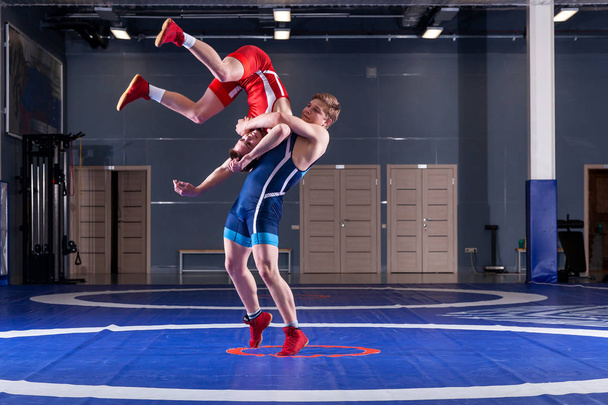 Koncept spravedlivého zápasu. Dva Greco-římští zápasníci v červené a modré uniformě na wrestlingový koberec v tělocvičně. Pojetí spravedlivého zápasu - Fotografie, Obrázek