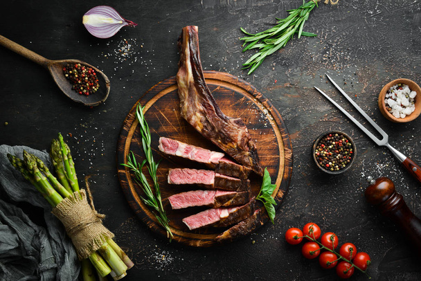 Grilled steak on the bone, herbs and spices on a wooden background. Barbecue. Top view. Free space for text. - Foto, Bild