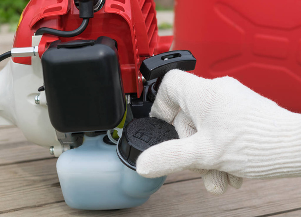 mão em luva fecha tanque de gasolina para cortador de grama, close-up
 - Foto, Imagem