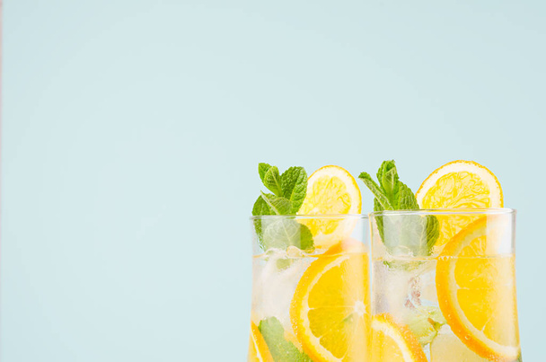 Fresh oranges cocktail with sliced fruit, ice cubes, mint on soft modern pastel green background, closeup, top section, edge. - Фото, изображение