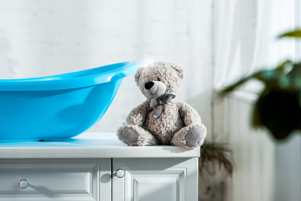 selective focus of teddy bear near blue baby bathtub in bathroom - Foto, Bild