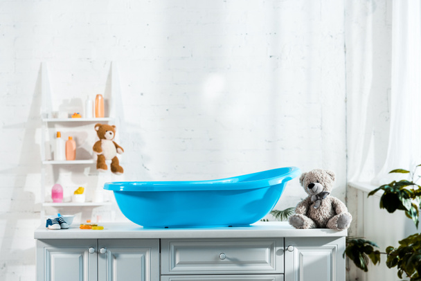 Blauwe baby bad in de buurt van Teddy Bear en baby sneakers in badkamer  - Foto, afbeelding